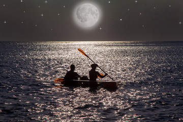 young couple canoeing in the ocean at night by the light of the big moon