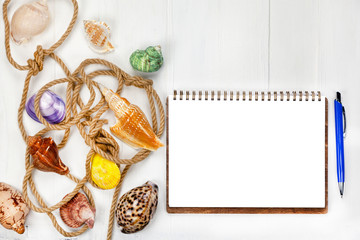 Summer vacation concept. Sea shells with rope on white wooden background, notebook with pen for summer plan, copy space.