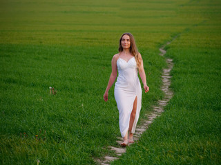 Obraz na płótnie Canvas girl in a long white dress on a green field