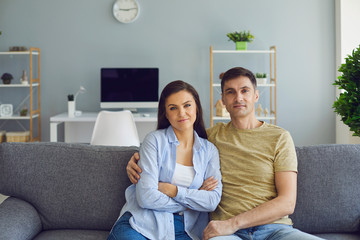 A couple in a serious emotional mood with problems looks at the camera while sitting on the couch.