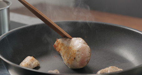 man hand turn over chicken fillet on non stick pan with wood spatula acloseup