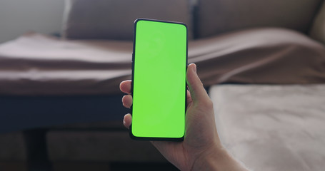 Closeup young man sit on a couch and show smartphone with green screen