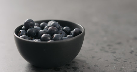 ripe blueberries in black bowl on concrete background with copy space