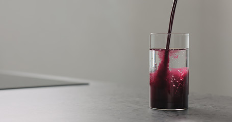 blueberry juice pour into water in highball glass on kitchen countertop
