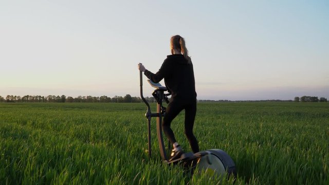Dolly shot. Green fitness. A young woman is working out on stepper in a green field.