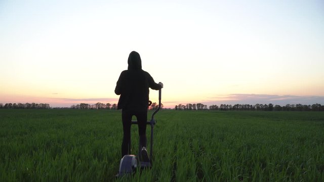 Dolly shot. Green fitness. A young woman is working out on stepper in a green field.