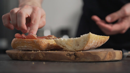 man add prosciutto on ciabatta on olive board