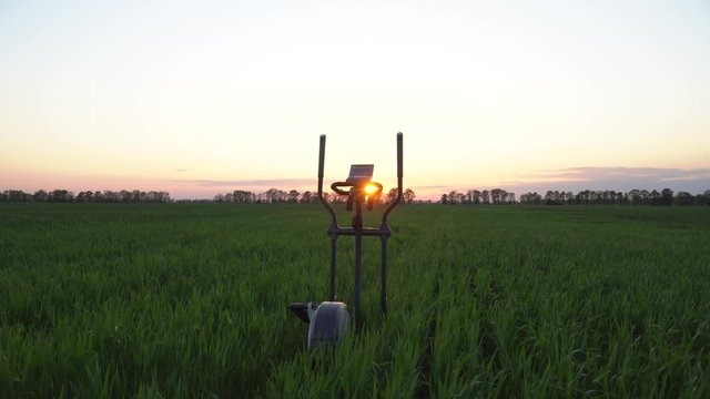 Fitness stopper orbitrek on a green field. Sunset. Dolly shot.