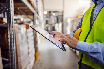 Closeup of employee in working vest using tablet to check on goods salary that day.