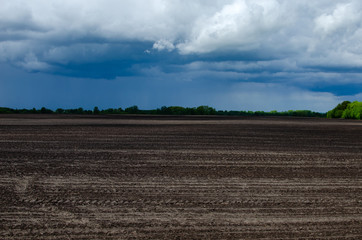 Plowed field in spring with thick thunderclouds and a cell tower on the horizon