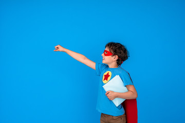 cheerful child dressed in superhero costume hold book and stretches out his hand
