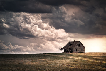 Old wooden farmhouse in the countryside at sunset with storm  clouds in the sky. There is a short grass meadow around the house. - obrazy, fototapety, plakaty