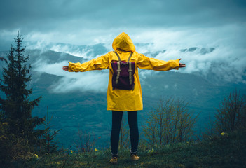 Woman hiker in yellow raincoat on mountain peak