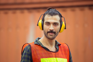 Cheerful factory worker man wearing noise reduction ear muffs and looking at camera with joy...