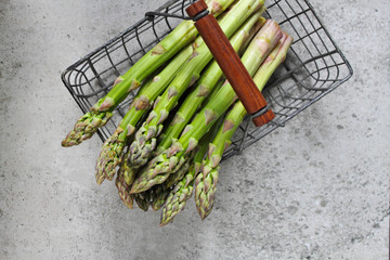 Banches of fresh green asparagus in an iron basket on a concrete background, top view