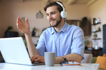 Happy young man in earphones working on laptop from home during self isolation.
