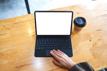 Top view mockup image of a hand using and touching tablet touchpad with blank white desktop screen as computer pc with coffee cup on the table