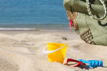 beach bag, bucket, rake and shovel on the beach sand, summer vacation concept