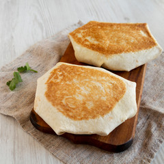 Homemade Beef Crunchwrap Quesadilla on a rustic wooden board on a white wooden background, side view.