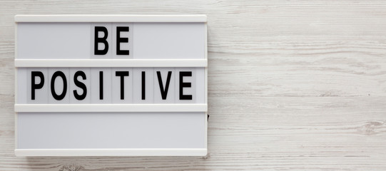 'Be positive' words on a lightbox on a white wooden surface, top view. Overhead, from above, flat lay. Space for text.