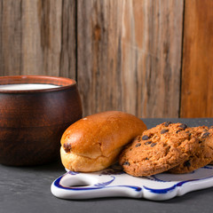 Breakfast, a chocolate bun, cookies and a mug of milk on a dark textured background