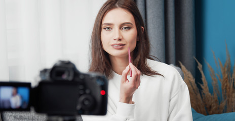 Portrait of young beauty blogger recording makeup tutorial applying lipstick or lip liner, front...