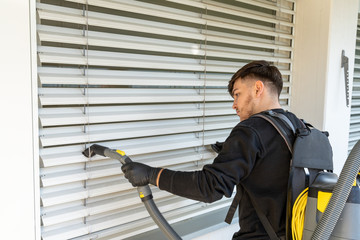 professional cleaner vacuum cleaning window blinds on an apartment balcony in a high-rise building
