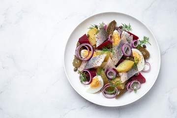 herring,  pickled cucumber, beet, potato and eggs salad on white  plate