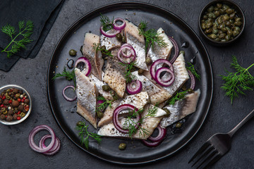pickled herring with  red onion, capers and dill on black plate