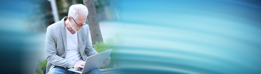 Mature businessman using laptop outdoors; panoramic banner
