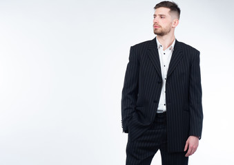 Portrait of a young man in a business suit. A bearded man on a white background. The man puts his hand in his pocket and looks away. Place for text.