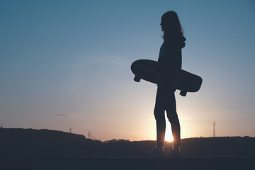 Silhouette of a young girl skater rides in a ramp in the outdoors area at dusk. Sport and outdoor concept.