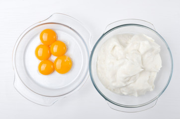 Top view of two glass bowls and separated yolk and egg whites on the bright kitchen table.Beaten egg whites and yolk