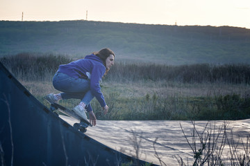 Young girl skater rides in a ramp in the outdoors area at dusk. Sport and outdoor concept.