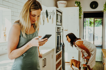 Daughter on smartphone while mother looks in oven