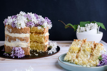 Biscuit cake with cream, impregnated with coconut and pineapple, decorated with lilac flowers.