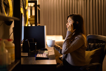 Young Asian woman talking on the phone while working from home late at night