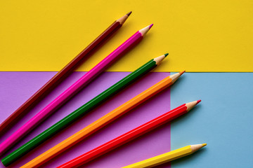 Multi-colored pencils lie on colorful sheets of paper. Bright background. Top view.