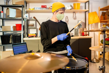 Young man in casualwear and protective mask and gloves hitting cymbals