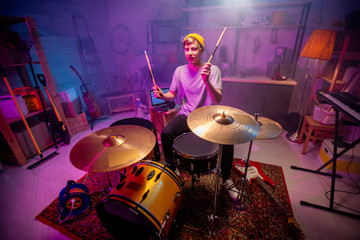 Young man in casualwear raising hands with drumsticks while going to hit cymbals