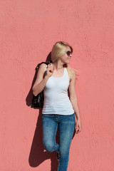 Obraz na płótnie Canvas outdoor summer portrait of young blonde cheerful woman with sunglasses and white tank top against pink wall mock up tank top