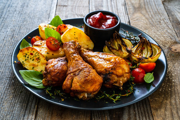 Barbecue chicken drumsticks with vegetables on wooden table
