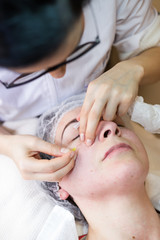 The treatment of the face in a spa by a female beautician. Extracting black dots or fat spots from a young woman's skin