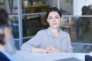 Pretty young brunette applicant in grey shirt looking at senior employer