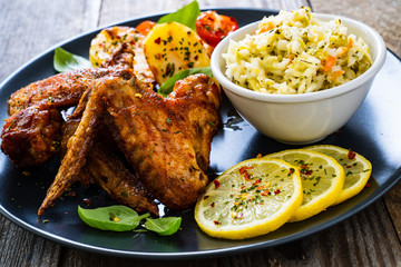 Roast chicken wings with potatoes and vegetable salad on wooden board
