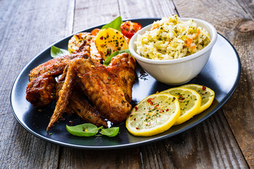 Roast chicken wings with potatoes and vegetable salad on wooden board
