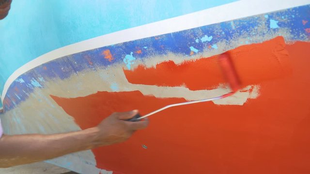 SLOW MOTION, CLOSE UP: Unrecognizable local man repaints his boat with bright red paint. Maldivian man does maintenance work on his boat. Dock worker performs upkeep on one of the colorful boats.