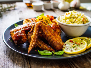 Roast chicken wings with potatoes and vegetable salad on wooden board
