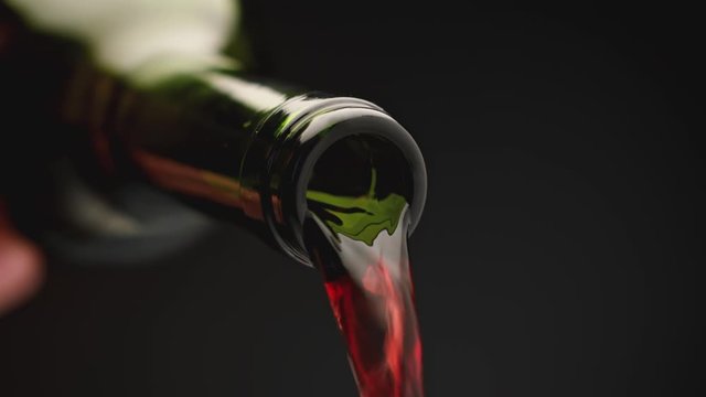 Red wine pours from the neck of bottle. Slow-motion pouring of red wine from a bottle, on a black background