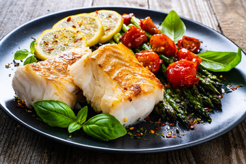 Fish dish - fried cod fillet with asparagus on wooden table
